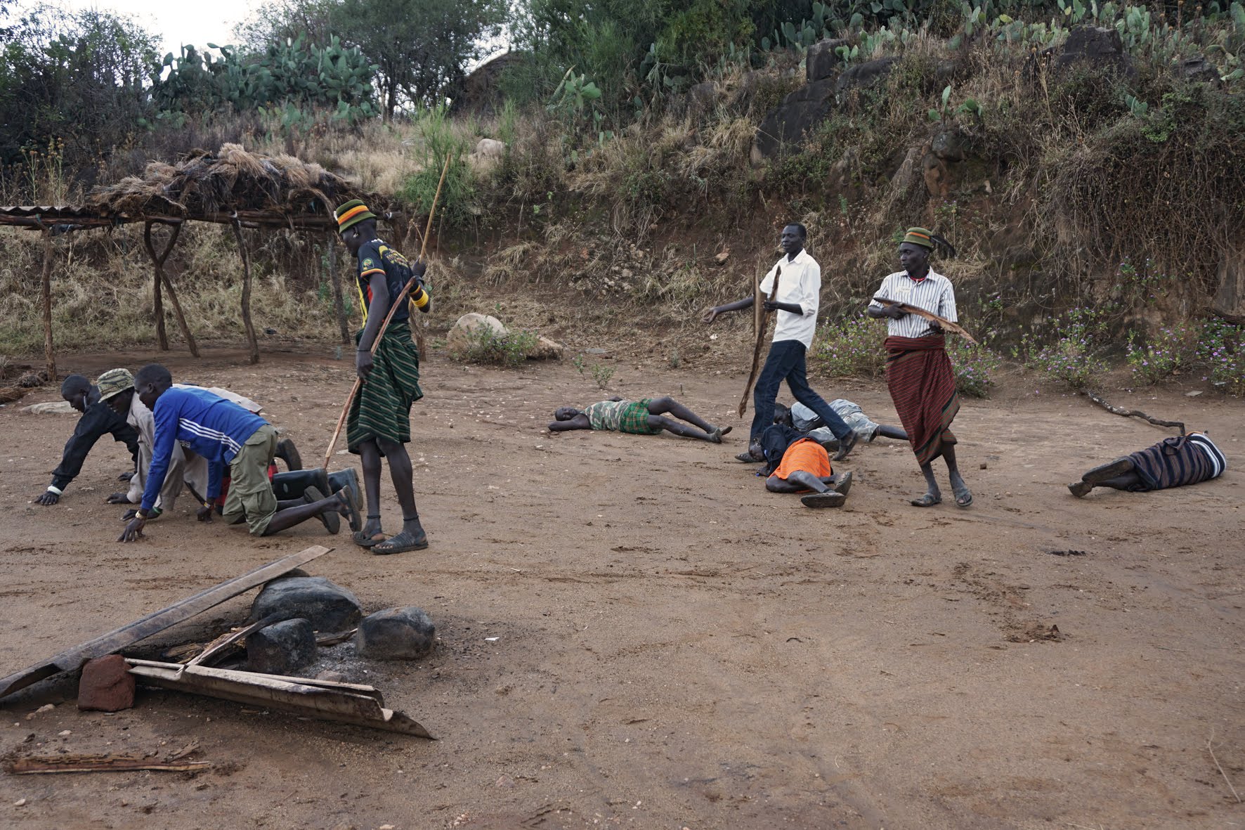 A scene re-enacting cattle theft with several tribal members lying on the ground, some walking on all fours representing cattle and some holding big branches, which represent guns.