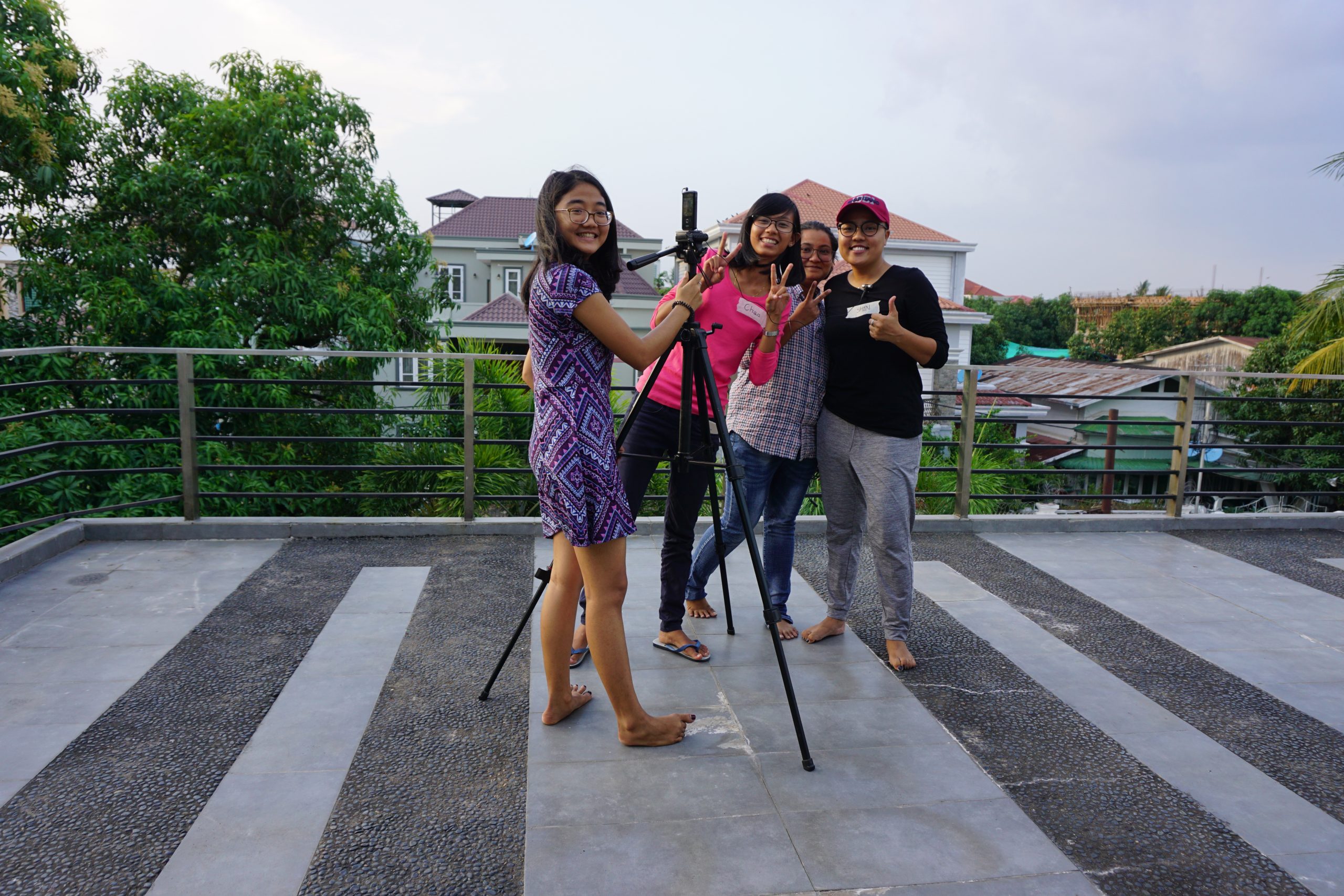 4 students are standing around a tripod with small camcorder set up on the roof terrace of Yangon Film School