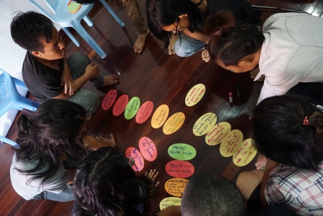 a group of students are squatting around an assembly of coloured oval paper shapes with all kinds of topics written on them