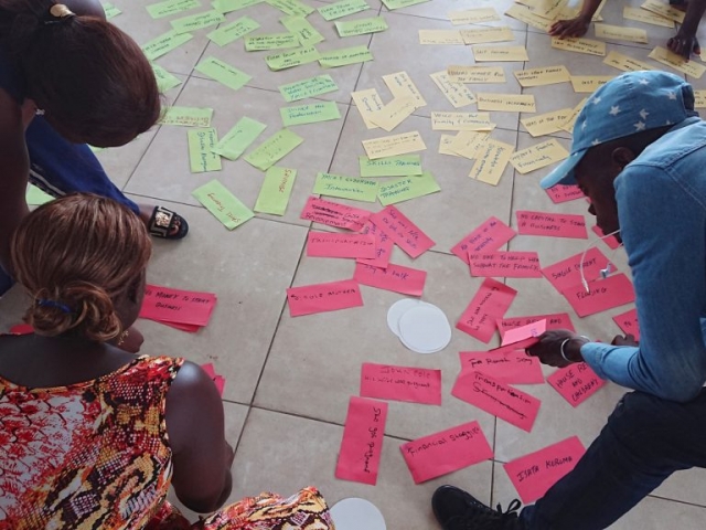 colourful paper shapes with words are lying on the floor while 3 young people search through them