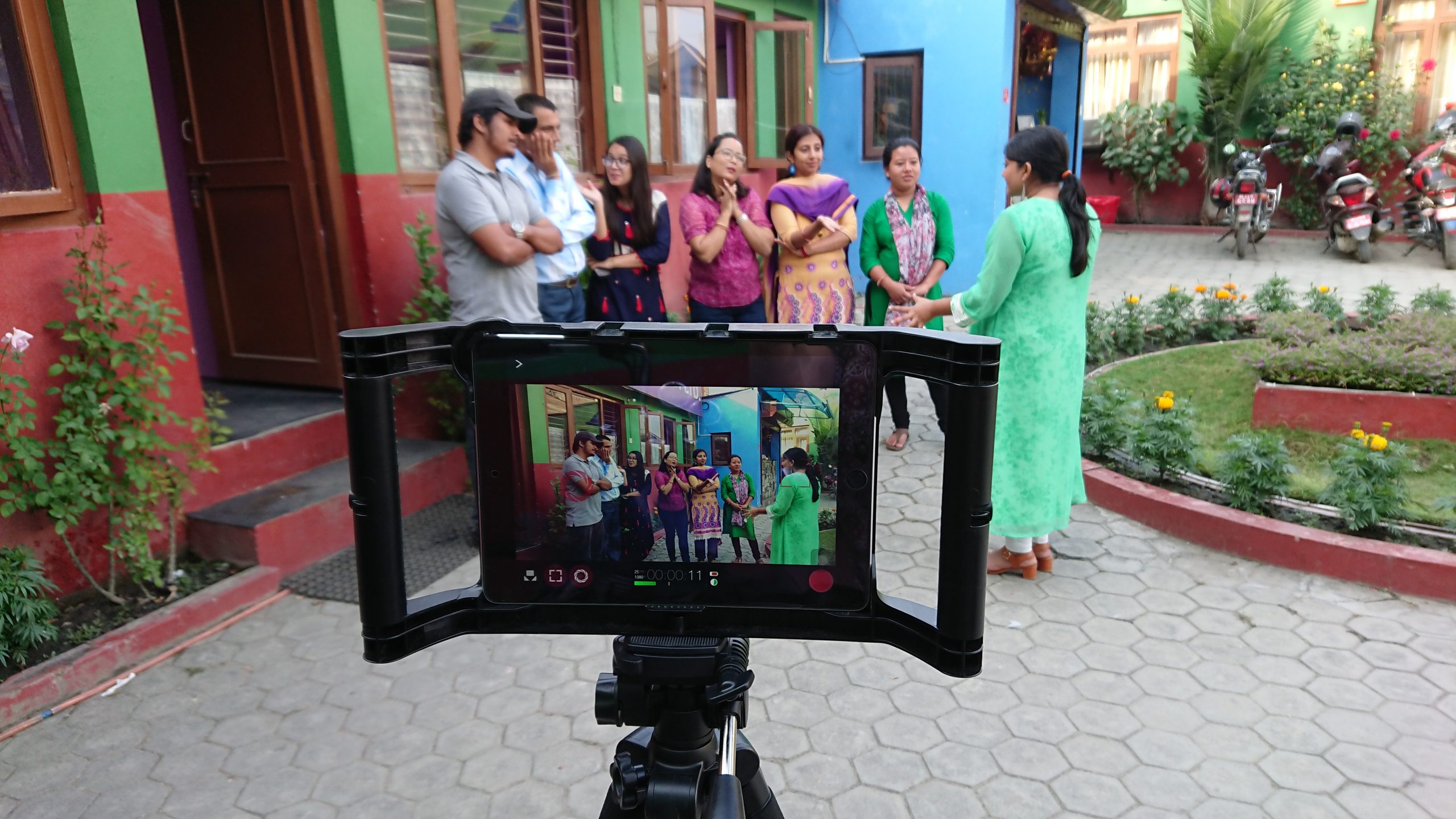 7 trainees stand in front of an iPad mounted on a tripod in a courtyard